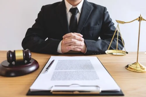 A personal injury lawyer sits at his desk with his hands folded across his chest.