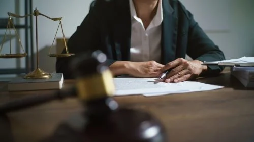 A personal injury lawyer writes with a grey pen at her desk with a gavel in the foreground.