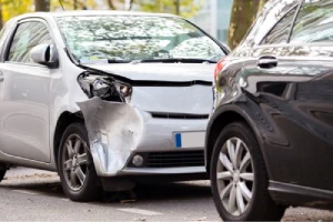 A silver rideshare car rearends a black car in the city.